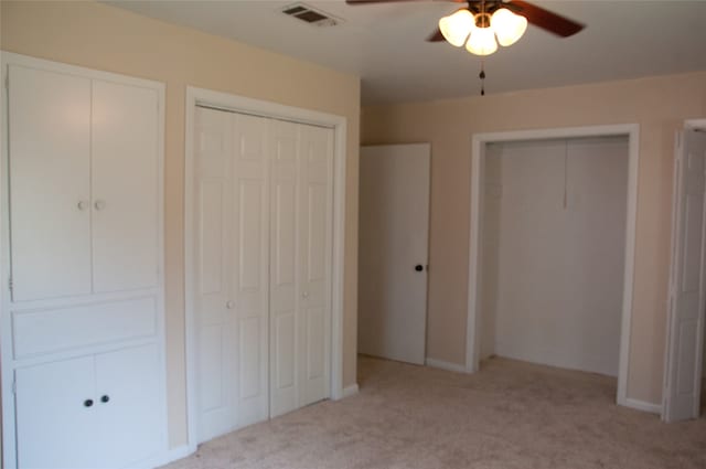 unfurnished bedroom featuring two closets, ceiling fan, and light carpet