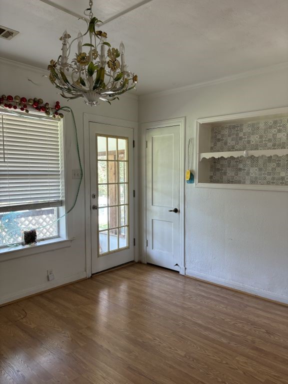 doorway to outside with a notable chandelier, hardwood / wood-style floors, and crown molding