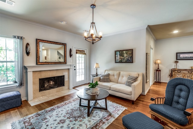 living room with a tiled fireplace, wood-type flooring, ornamental molding, and an inviting chandelier