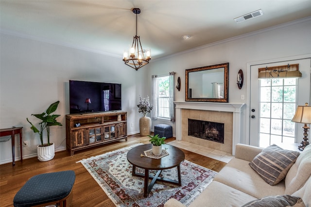 living room featuring a notable chandelier, ornamental molding, a tiled fireplace, and wood-type flooring