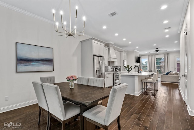 dining space with sink, ceiling fan with notable chandelier, crown molding, and dark wood-type flooring