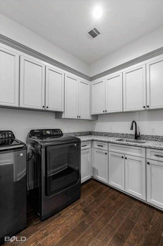 clothes washing area with washing machine and clothes dryer, cabinets, sink, and dark wood-type flooring