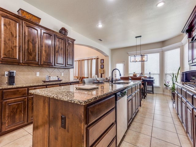 kitchen featuring light stone counters, sink, a center island with sink, decorative light fixtures, and stainless steel dishwasher