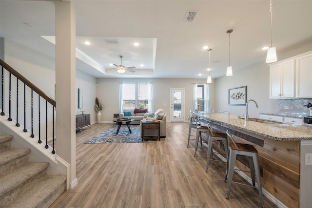 interior space featuring ceiling fan, light hardwood / wood-style flooring, sink, and a tray ceiling