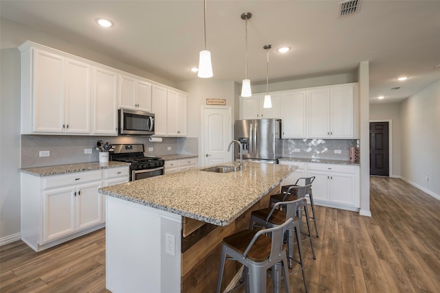 kitchen featuring appliances with stainless steel finishes, a kitchen island with sink, tasteful backsplash, sink, and wood-type flooring