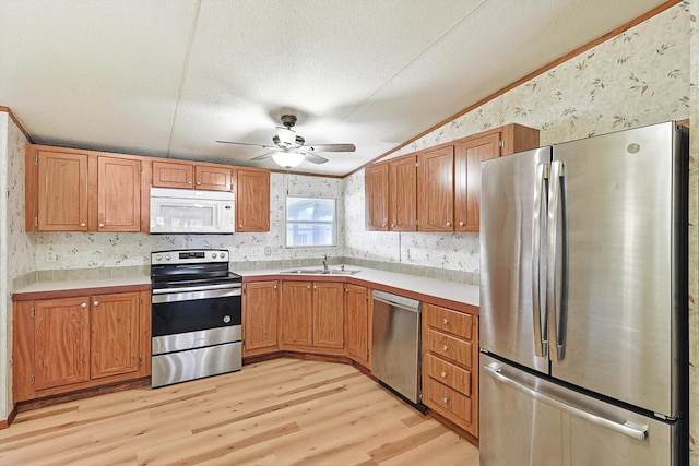 kitchen featuring ceiling fan, appliances with stainless steel finishes, vaulted ceiling, light wood-type flooring, and sink