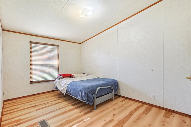 bedroom featuring a textured ceiling, light wood-type flooring, and crown molding