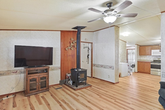 living room featuring ceiling fan, a wood stove, light hardwood / wood-style flooring, and a textured ceiling