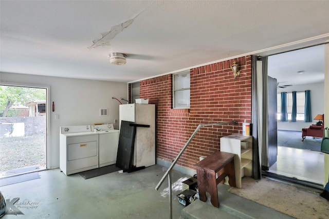 interior space featuring washing machine and dryer, white refrigerator, a healthy amount of sunlight, and brick wall