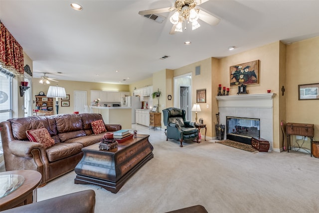 living room with a tiled fireplace, ceiling fan, and light carpet