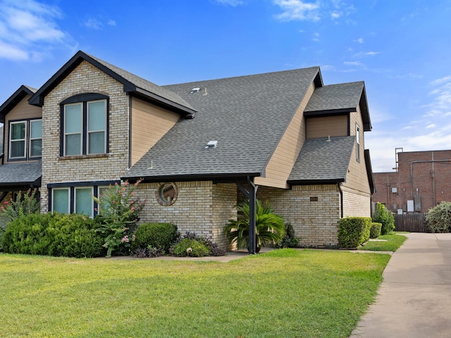 view of front of house with a shingled roof, a front yard, and brick siding