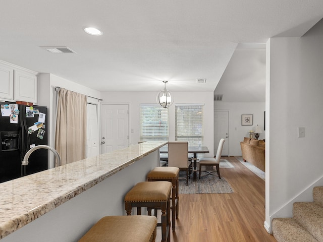 kitchen featuring a breakfast bar, visible vents, black refrigerator with ice dispenser, light wood-style floors, and white cabinets