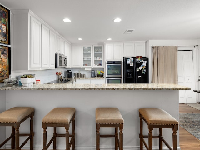 kitchen featuring a breakfast bar area, a peninsula, white cabinets, black appliances, and glass insert cabinets