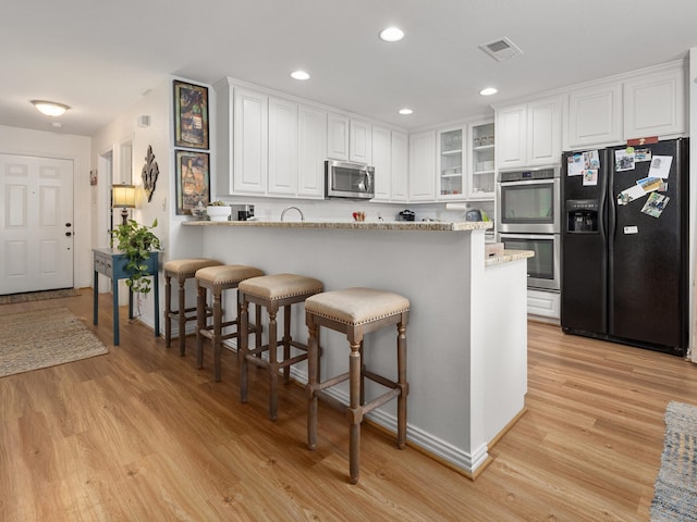 kitchen with stainless steel appliances, visible vents, light wood-style floors, white cabinets, and a kitchen breakfast bar