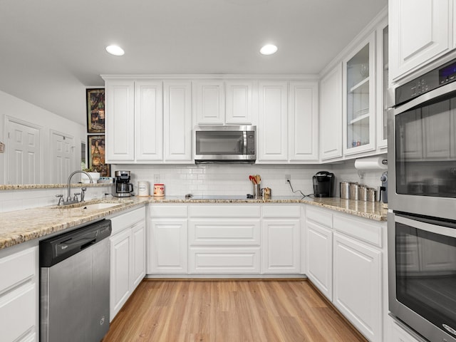 kitchen with tasteful backsplash, white cabinets, light wood-style flooring, stainless steel appliances, and a sink