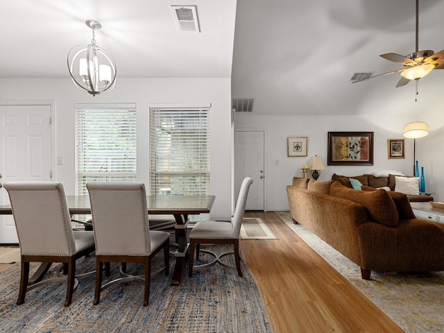 dining room featuring ceiling fan with notable chandelier, visible vents, vaulted ceiling, and wood finished floors