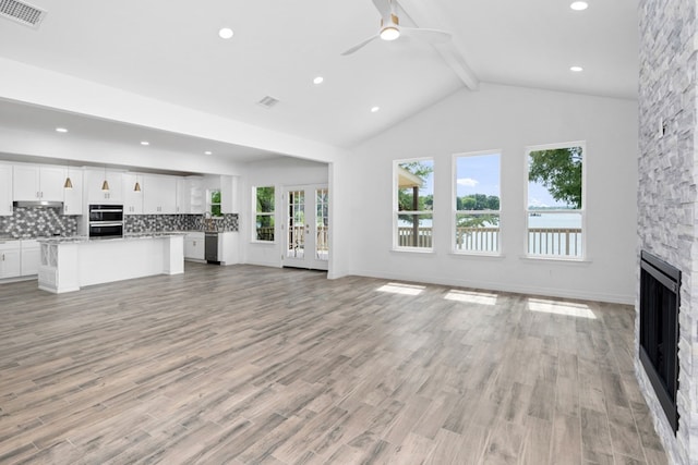 unfurnished living room with ceiling fan, light hardwood / wood-style flooring, beamed ceiling, and a stone fireplace