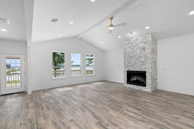 unfurnished living room featuring ceiling fan, wood-type flooring, vaulted ceiling with beams, and a stone fireplace