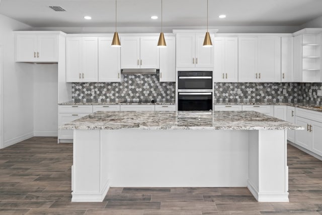 kitchen with stainless steel double oven, backsplash, a center island, white cabinets, and decorative light fixtures