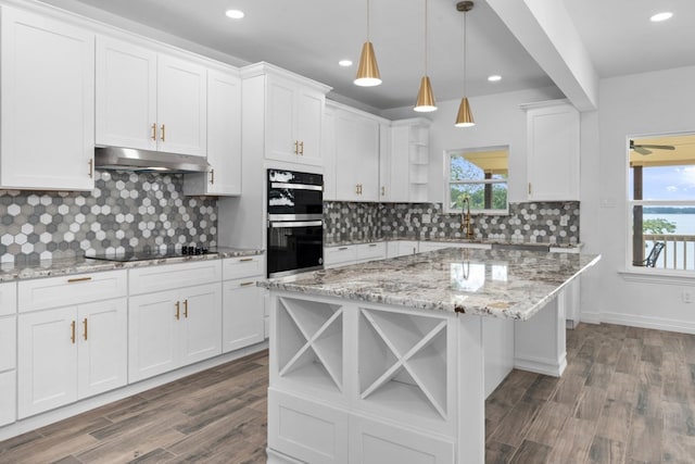 kitchen featuring multiple ovens, plenty of natural light, decorative backsplash, dark wood-type flooring, and wall chimney exhaust hood