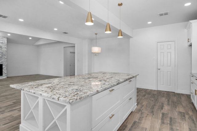 kitchen with dark wood-type flooring, a stone fireplace, hanging light fixtures, a kitchen island, and white cabinetry