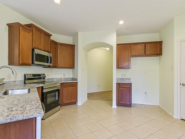 kitchen with appliances with stainless steel finishes, sink, light tile patterned floors, and light stone countertops