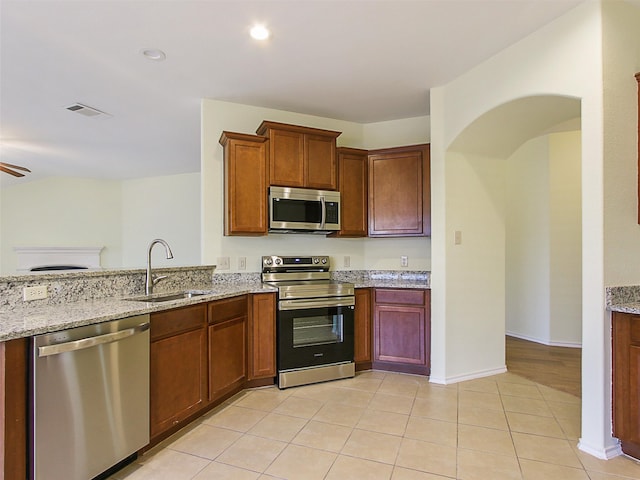 kitchen with sink, stainless steel appliances, light hardwood / wood-style flooring, and light stone counters