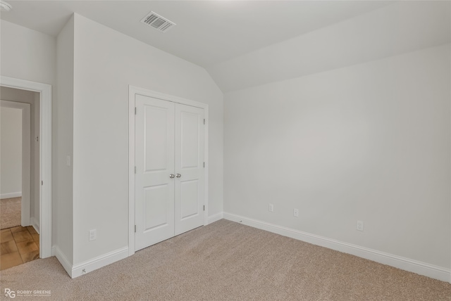 unfurnished bedroom featuring carpet floors, lofted ceiling, and a closet