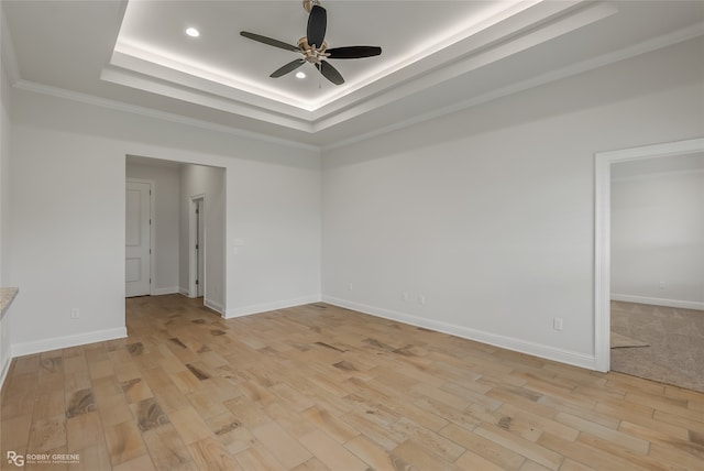 spare room featuring a raised ceiling, light hardwood / wood-style floors, crown molding, and ceiling fan