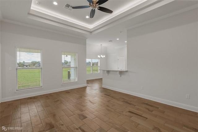 unfurnished living room with ceiling fan with notable chandelier, wood-type flooring, a tray ceiling, and crown molding