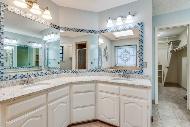 bathroom featuring a skylight, vanity, a textured ceiling, a shower with shower door, and tile patterned flooring