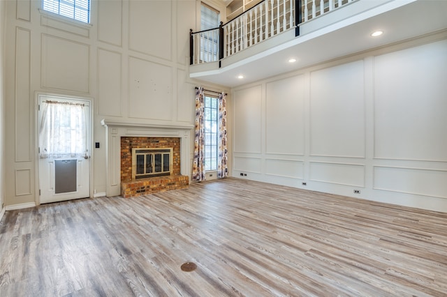 unfurnished living room featuring a high ceiling, light hardwood / wood-style flooring, and a brick fireplace