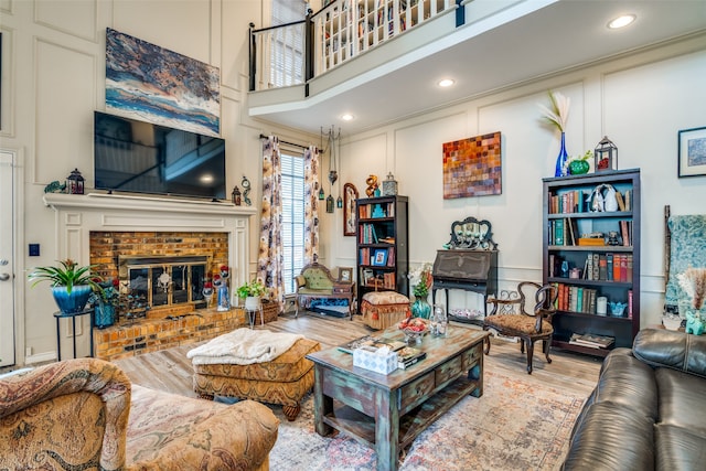 living room featuring a brick fireplace, light hardwood / wood-style flooring, and a towering ceiling