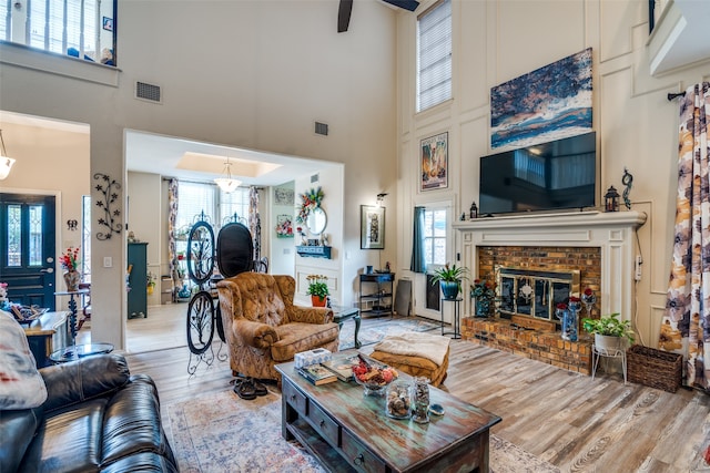 living room with a brick fireplace, light wood-type flooring, and a towering ceiling