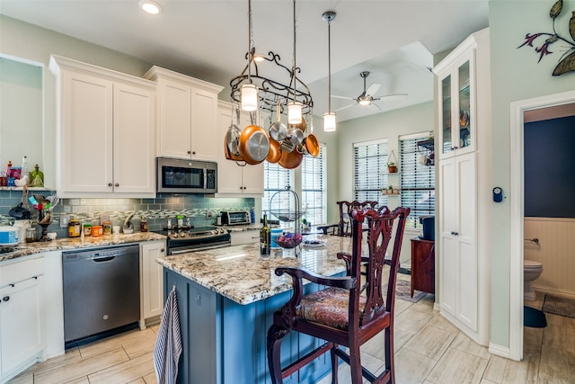 kitchen featuring appliances with stainless steel finishes, white cabinetry, an island with sink, and light stone counters