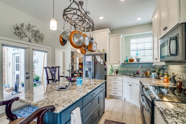 kitchen featuring a center island, white cabinetry, hanging light fixtures, appliances with stainless steel finishes, and light stone countertops