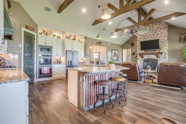 kitchen featuring an island with sink, decorative light fixtures, light stone counters, and a breakfast bar