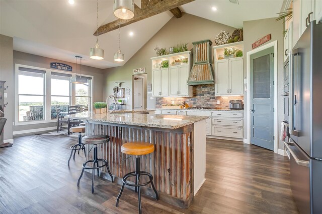 kitchen featuring an island with sink, hanging light fixtures, beam ceiling, dark wood-type flooring, and light stone countertops