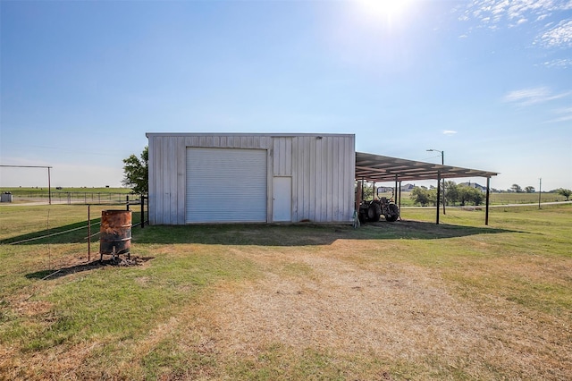 view of outdoor structure with a rural view, a garage, a yard, and a carport