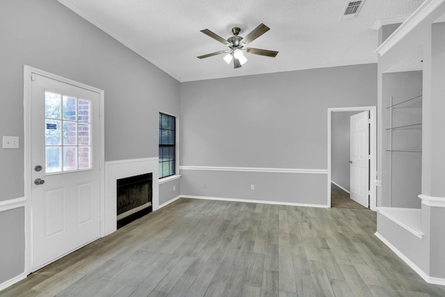 unfurnished living room with a fireplace, crown molding, visible vents, ceiling fan, and wood finished floors