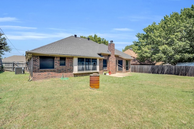 back of house featuring a yard, brick siding, a chimney, and a fenced backyard