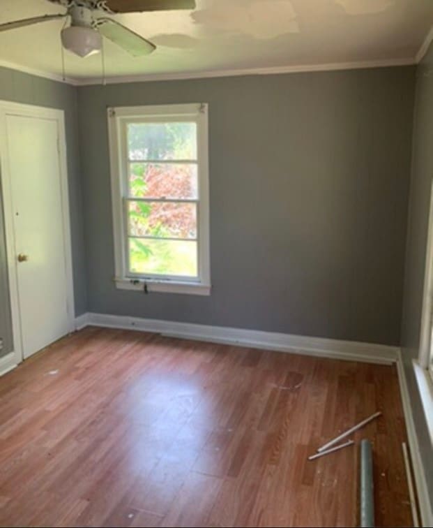 empty room with ceiling fan, wood-type flooring, and crown molding