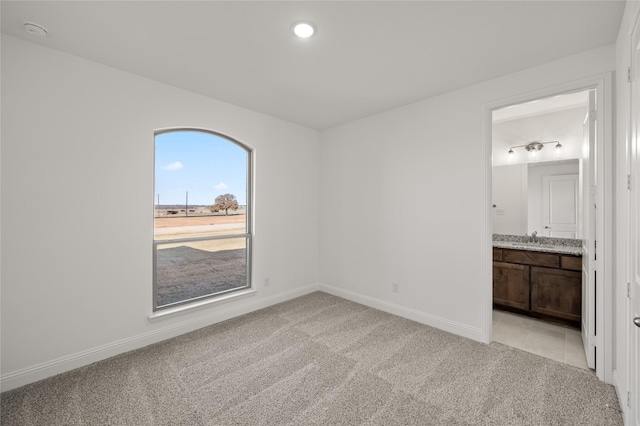 unfurnished bedroom featuring light colored carpet, sink, and ensuite bath