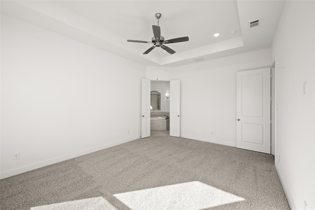 unfurnished bedroom with a raised ceiling, ceiling fan, carpet, and connected bathroom