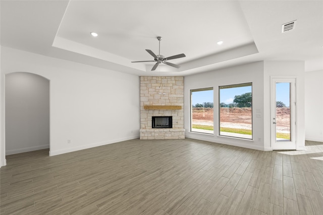 unfurnished living room with ceiling fan, a tray ceiling, and a stone fireplace