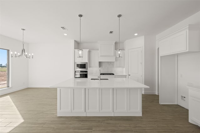 kitchen featuring a kitchen island with sink, built in microwave, oven, white cabinets, and sink