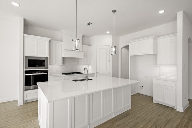 kitchen featuring white cabinetry, a kitchen island with sink, built in microwave, oven, and sink