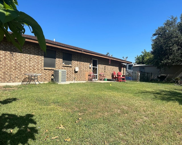 rear view of house with brick siding, central AC, and a yard