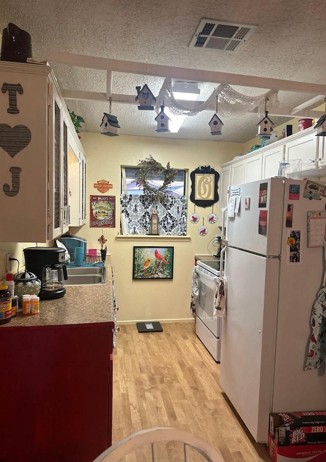 kitchen with white appliances, visible vents, white cabinets, a textured ceiling, and light wood-style floors