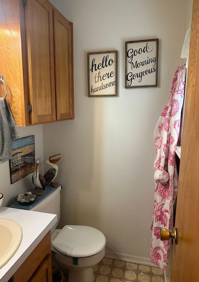 half bathroom with baseboards, vanity, and toilet